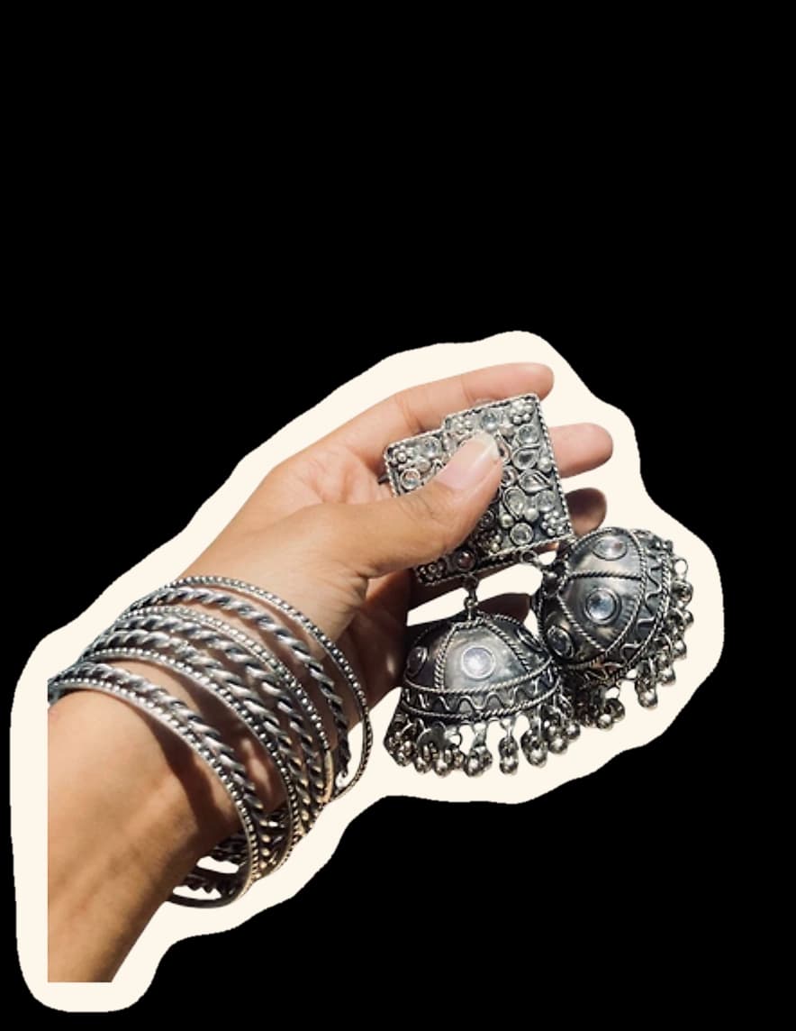 A hand stacked with bangles, holding a pair of oxidised jhumkas